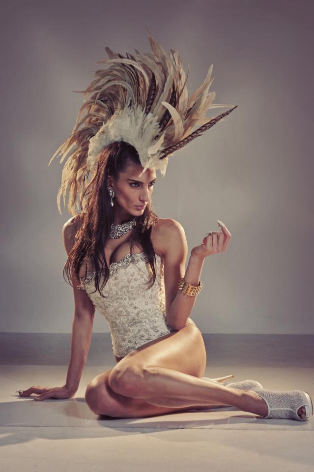 Light-skinned woman sitting on the floor wearing a large feather head piece and a Deborah Brand Anoushka bridal corset.