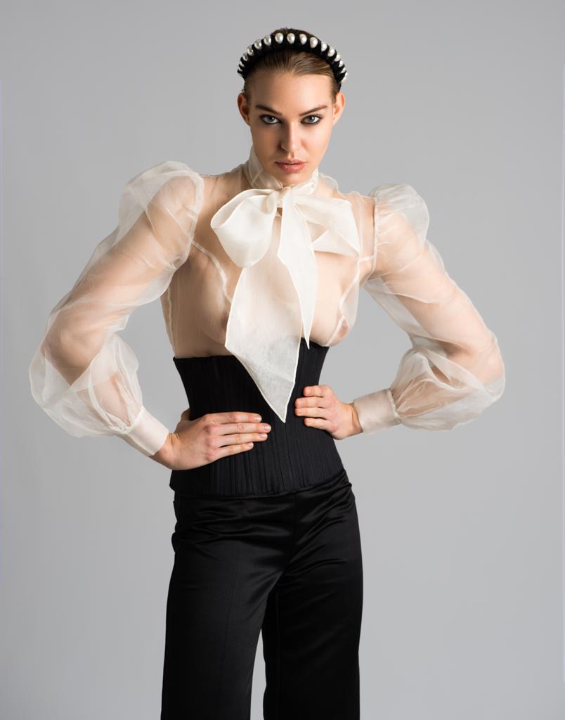 A light-skinned woman wearing a black Mila corset with black trousers and a cream blouse. 